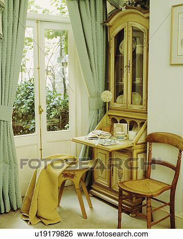 Stock Photograph - Antique bureau beside French doors with pastel green curtains. Fotosearch