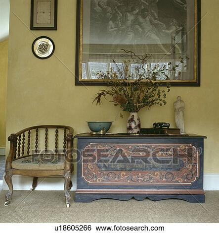 Stock Photograph - Antique chair and painted wooden chest below large picture in neutral hall. Fotosearch
