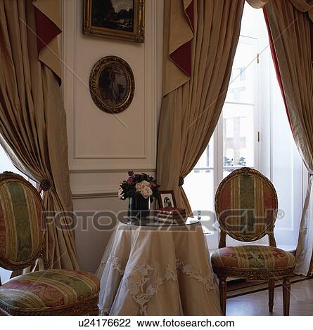 Antique chairs and table with appliqued circular cloth in cream bedroom with swagged and tailed cream curtains View Large Photo Image Stock Image - Antique chairs and table with appliqued circular cloth in cream bedroom with swagged and tailed cream curtains . Fotosearch