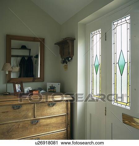 Stock Image - Antique chest of drawers beside front door with stained glass panels. Fotosearch