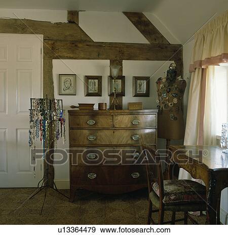 Antique chest of drawers in beamed cottage bedroom with necklaces on stand View Large Photo Image Stock Photo - Antique chest of drawers in beamed cottage bedroom with necklaces on stand. Fotosearch