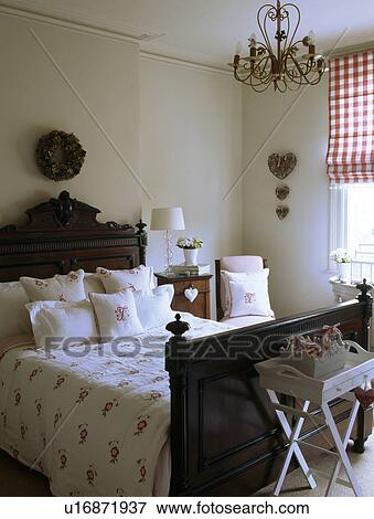Antique mahogany bed with monogrammed linen cushions and floral quilt in bedroom with red+white checked blind View Large Photo Image Stock Photo - Antique mahogany bed with monogrammed linen cushions and floral quilt in bedroom with red+white checked blind. Fotosearch
