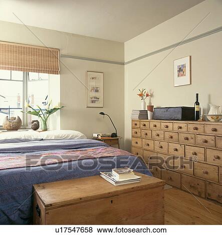 Stock Photo - Antique pine merchant's chest in modern bedroom with split-cane blind and pine chest at the end of the bed. Fotosearch