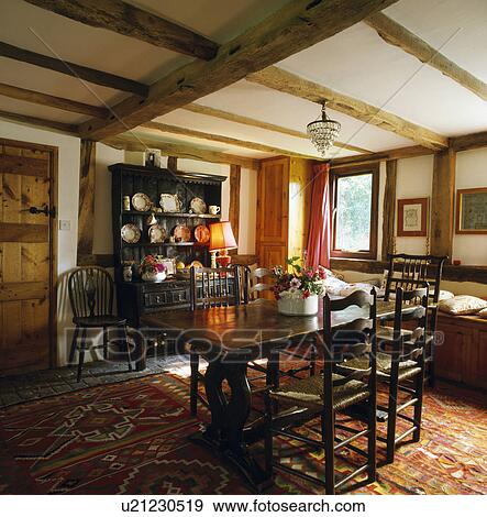 Stock Photo - Antique rectangular table and rush-seated chairs in country diningroom with Kelim rug on floor and beamed ceiling. Fotosearch