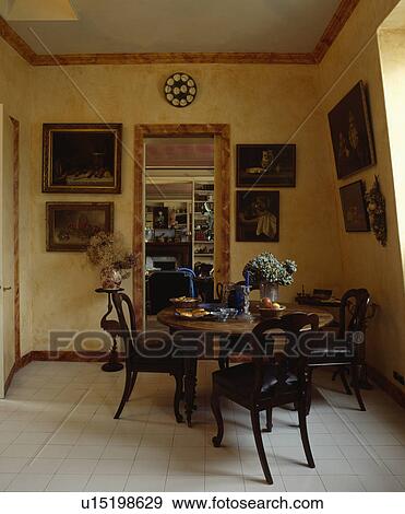 Stock Photo - Antique table and chairs in dining room with white floor tiles and pictures on paint effect walls. Fotosearch