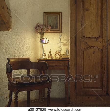 Antique wooden chair and table with lighted lamp beside old carved wooden doors on built-in cupboard in cottage hall View Large Photo Image Stock Photo - Antique wooden chair and table with lighted lamp beside old carved wooden doors on built-in cupboard in cottage hall. Fotosearch