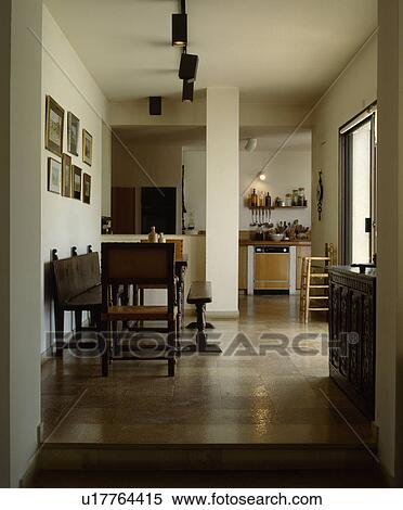 Stock Photography - Antique wooden chairs and bench with table in openplan dining room and kitchen with tiled floor. Fotosearch