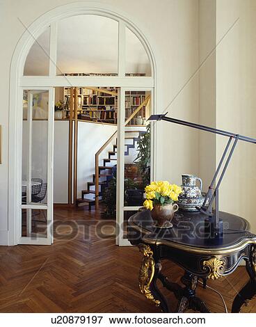 Artemide lamp on antique table in hall with parquet flooring and arched glass doors to dining room View Large Photo Image Stock Photo - Artemide lamp on antique table in hall with parquet flooring and arched glass doors to dining room. Fotosearch