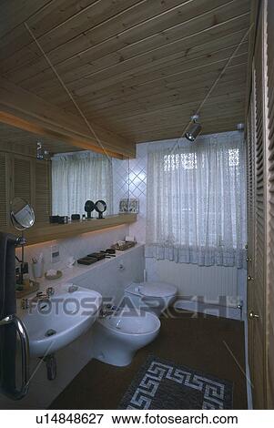 Stock Photo - Basin and wall-mounted basin in small bathroom with white net curtains and wooden ceiling . Fotosearch