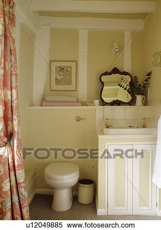 Stock Photography - Basin in vanity unit beside toilet in cream cottage bathroom with white beams. Fotosearch
