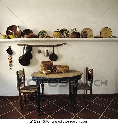 Baskets and pottery plates on shelf in kitchen with circular wooden table and antique chairs on tiled floor View Large Photo Image Stock Image - Baskets and pottery plates on shelf in kitchen with circular wooden table and antique chairs on tiled floor. Fotosearch