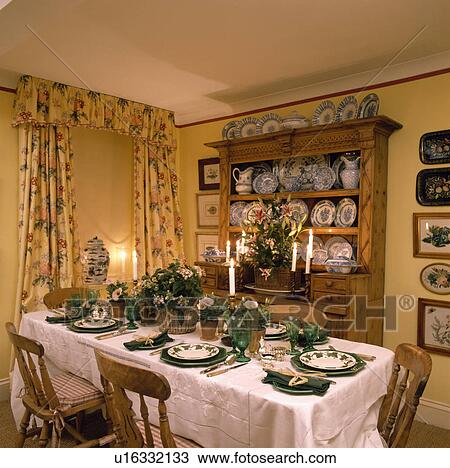 Baskets of flowers and green plates on white tablecloth in yellow dining room with dresser and yellow floral curtains View Large Photo Image Stock Image - Baskets of flowers and green plates on white tablecloth in yellow dining room with dresser and yellow floral curtains. Fotosearch