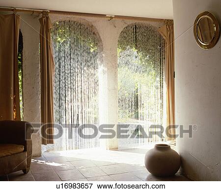 Stock Photo - Beaded curtains on arched doorways in French country hall. Fotosearch