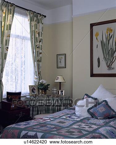Stock Image - Bed with cushions and patchwork quilt in small bedroom. Fotosearch