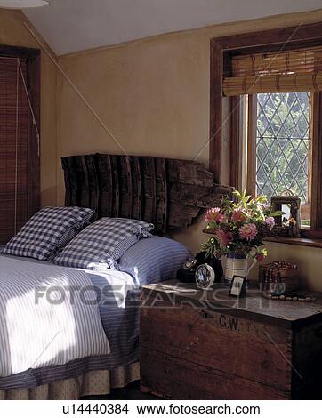 Picture - Bedroom with wooden chest beside bed with blue+white cushions and salvaged rustic wooden headboard . Fotosearch
