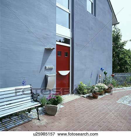 Stock Photo - Bench on patio outside modern grey house with red front door. Fotosearch
