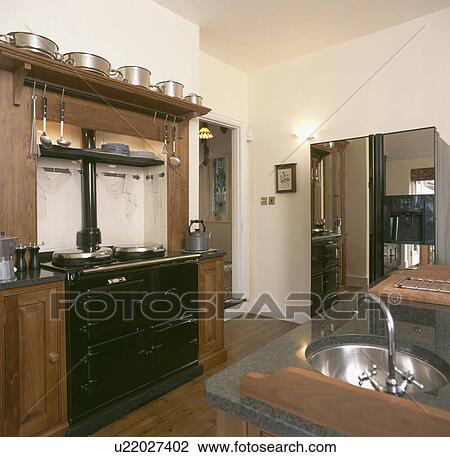Stock Image - Black Aga and large refrigerator in kitchen with circular stainless steel sink. Fotosearch