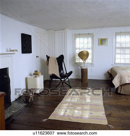 Stock Photo - Black Butterfly chair and patterned cream Ikat rug in white bedroom with modern sculpture and old wooden floorboards. Fotosearch