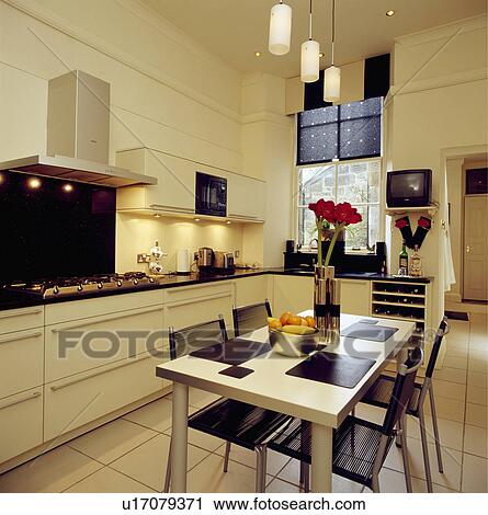 Black chairs and rectangular table below cylindrical pendant lights in cream kitchen with black blind and white floor tiles View Large Photo Image Stock Image - Black chairs and rectangular table below cylindrical pendant lights in cream kitchen with black blind and white floor tiles. Fotosearch