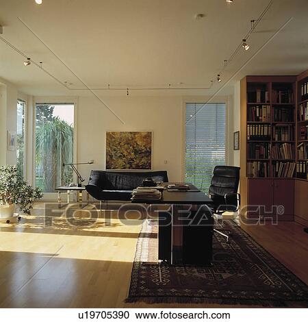 Stock Image - Black desk and black leather chair in home office in corner of modern living room. Fotosearch