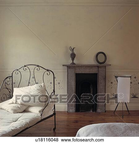 Black wrought-iron antique daybed in simple white bedroom with stone fireplace and wooden flooring View Large Photo Image Stock Photo - Black wrought-iron antique daybed in simple white bedroom with stone fireplace and wooden flooring. Fotosearch
