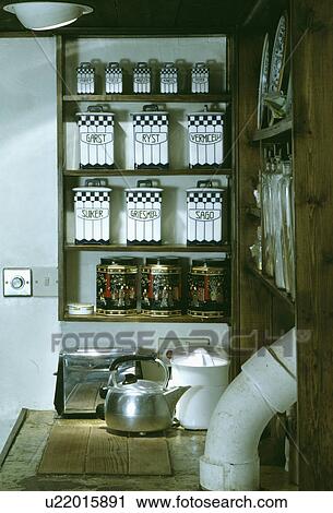 Stock Image - Black+white ceramic storage jars on shelves above old patterned tins and chrome toaster and kettle. Fotosearch