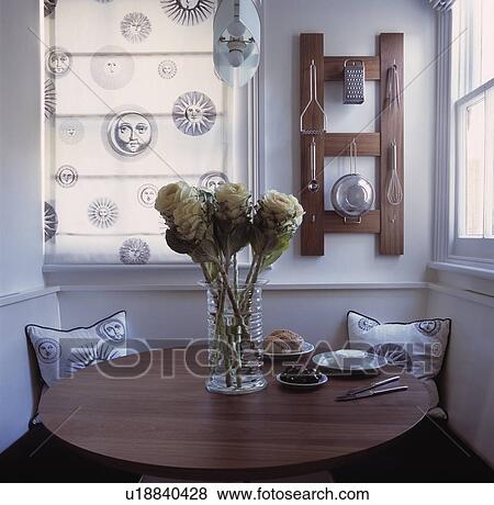 Black+white Fornasetti print blind and cushions in white dining room with faux roses in glass vase on wood table View Large Photo Image Stock Photo - Black+white Fornasetti print blind and cushions in white dining room with faux roses in glass vase on wood table. Fotosearch