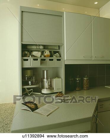 Picture - Blenders and mixers stored in cupboard with fold-up door in modern grey kitchen. Fotosearch