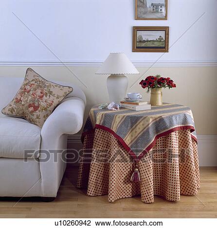 Stock Image - Blue and white patterned cloths on circular table beside white sofa in traditional livingroom. Fotosearch
