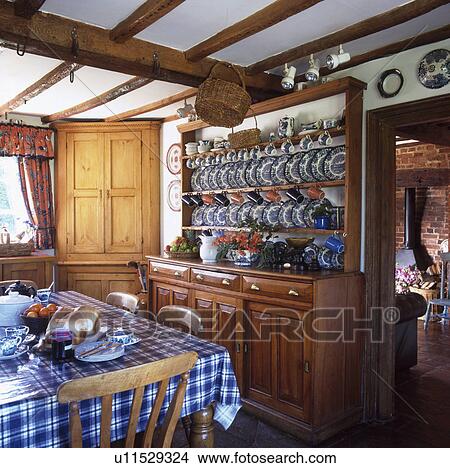 Picture - Blue and white plates on dresser in cottage kitchen with blue checked cloth on the table. Fotosearch