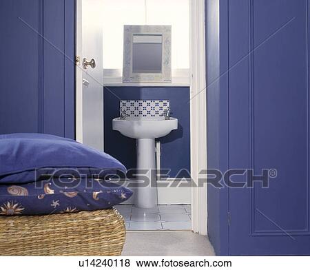 Stock Photo - Blue cushions on basket in front of blue cupboards and door open to white pedestal basin in bathroom. Fotosearch