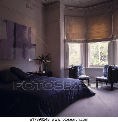 Blue Quilt On Double Bed In Modern Bedroom With Cream Blinds At Bay Window And Grey Carpet Stock Photo