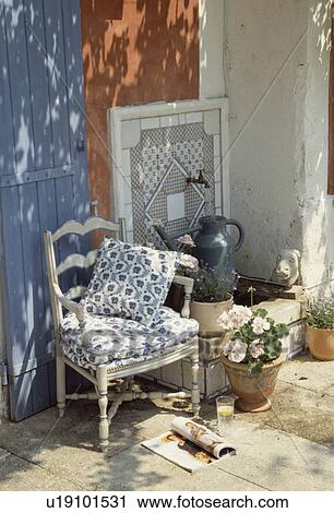Stock Image - Blue+white cushions on old chair beside tap in tiled wall in Mediterranean garden. Fotosearch