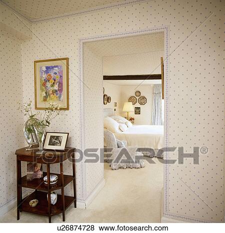 Stock Photo - Blue+white spotted wallpaper on landing with tiered table beside open door to traditional bedroom with cream carpet. Fotosearch