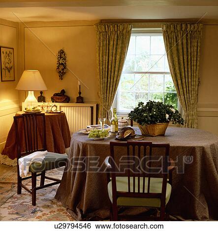 Stock Photograph - Brown cloths on side table and dining table in dining room with lighted lamp in corner of the room. Fotosearch