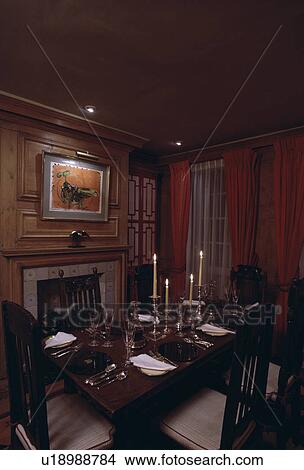 Picture - Candlesticks and place settings on antique table in dark dining room. Fotosearch