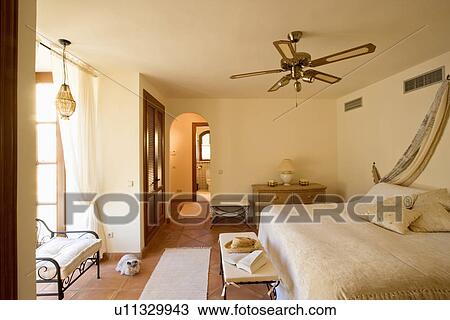 Stock Image - Ceiling fan above bed with cream bedcover in bedroom in Spanish apartment. Fotosearch