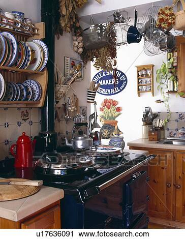 Stock Image - Ceramic plates on rack above black Aga with red coffeepot . Fotosearch