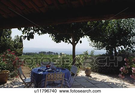 Stock Image - Chairs and table with white cloth on terrace of house in Provence. Fotosearch