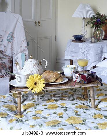 Stock Image - China teapot with croissants on cane tray on bed with yellow+white floral duvet. Fotosearch