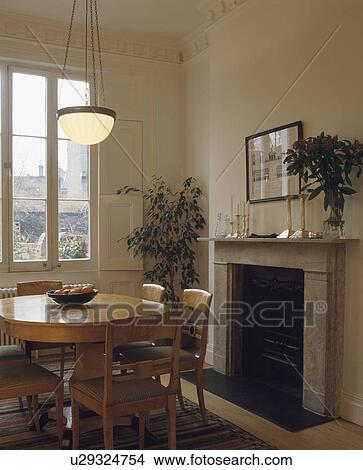 Picture - Circular polished walnut table and chairs in diningroom with marble fireplace. Fotosearch