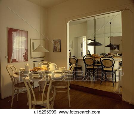 Circular table set for breakfast and white bentwood chairs in dining room beside doorway to large kitchen View Large Photo Image Stock Photo - Circular table set for breakfast and white bentwood chairs in dining room beside doorway to large kitchen. Fotosearch