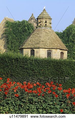 Stock Image - Clipped hedge in front of stone dovecot in large country garden in summer. Fotosearch