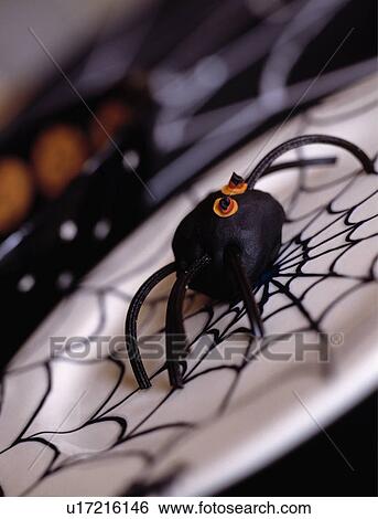 Stock Photograph - Close-up of black fabric spider on white plate decorated with Halloween motif. Fotosearch
