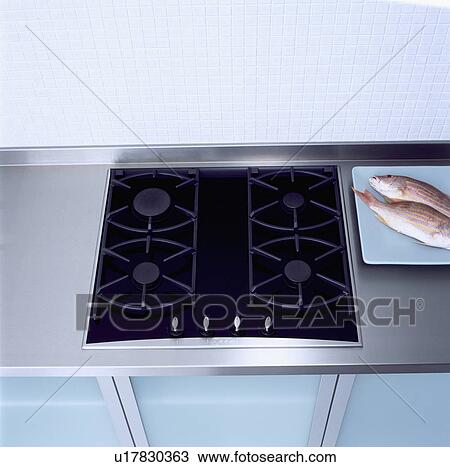 Stock Image - Close-up of black gas hob in stainless steel worktop with fish on plate&#13; &#10; &#13; &#10; &#13; &#10; &#13; &#10; &#13; &#10; &#13; &#10;. Fotosearch