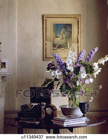 Stock Photo - Close-up of blue and white delphiniums and wooden box and clock on table below picture on wall. Fotosearch