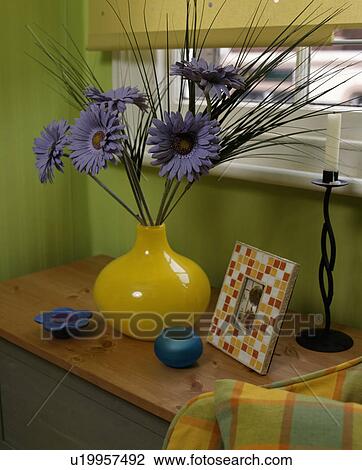 Stock Image - Close-up of blue plastic flowers in yellow vase. Fotosearch