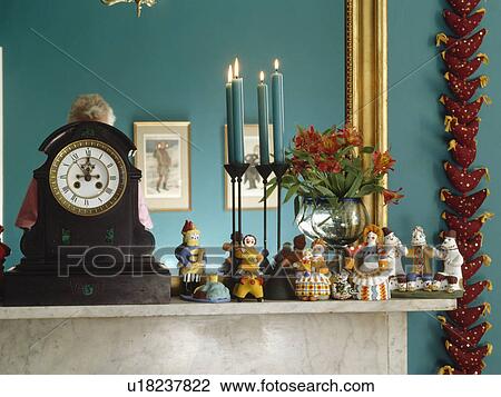 Stock Image - Close-up of clock and ceramic folk ornaments on mantelpiece. Fotosearch
