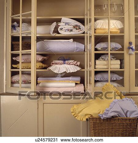 Stock Image - Close-up of cupboard with glazed doors open to sheets and pillows on shelves. Fotosearch