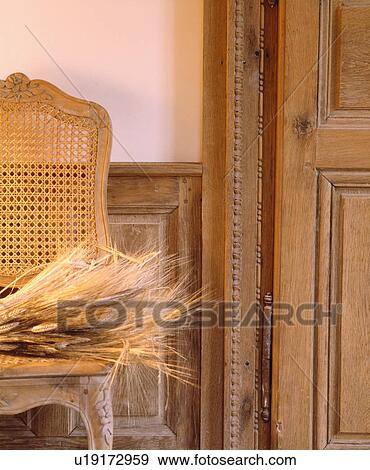 Stock Photo - Close-up of dried grasses on antique chair beside old carved wooden door. Fotosearch